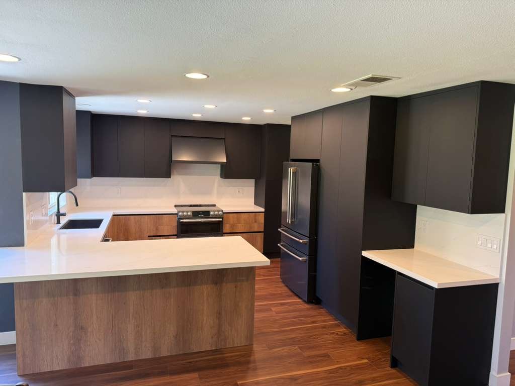 Completed modern kitchen with wood flooring, flat panel cabinetry, island seating, integrated appliances, and contemporary lighting.