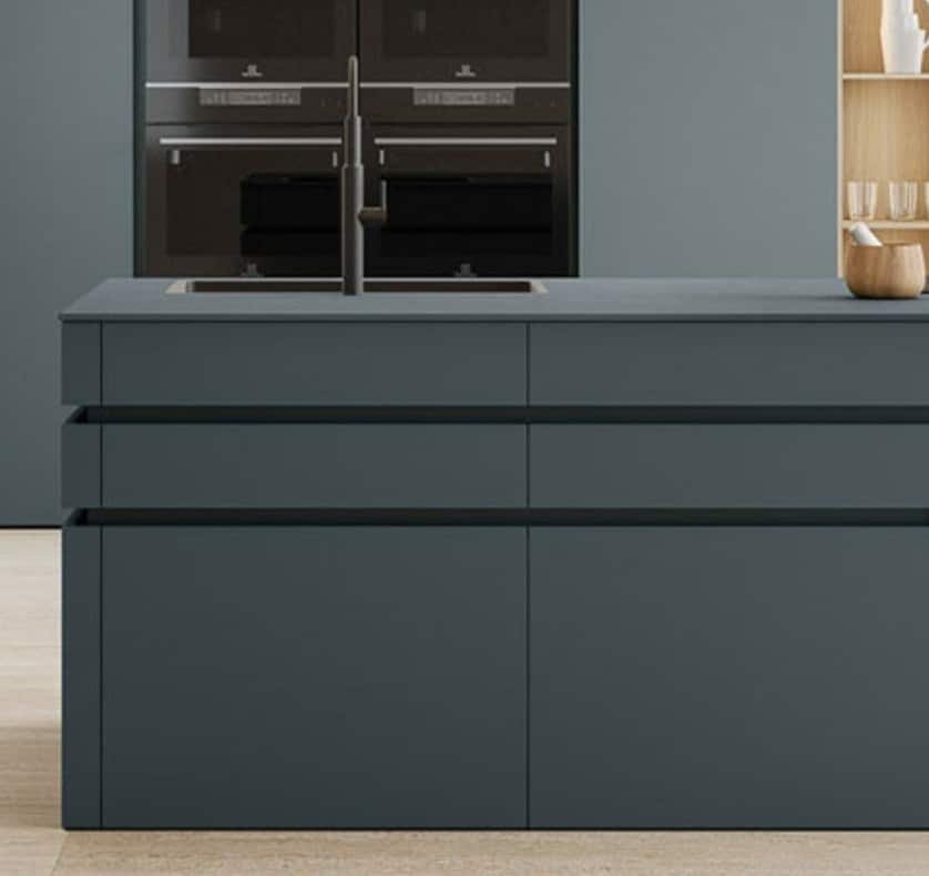 Sleek matte lacquer kitchen island in a deep blue green finish with handleless drawers, integrated sink, and modern built-in appliances.