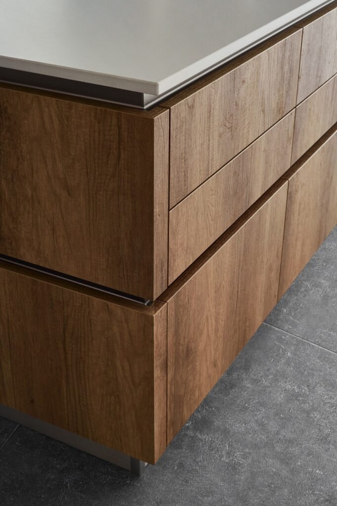 Close-up of warm wood textured melamine cabinet drawers with clean horizontal lines, integrated handle detailing, and modern kitchen styling.