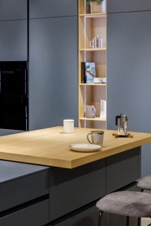 Contemporary Italian kitchen showroom featuring custom blue cabinetry, wood peninsula countertop, and integrated storage solutions.