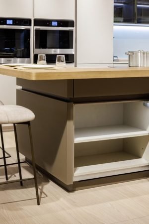 Contemporary Italian kitchen with a central island, integrated open shelving, beige cabinetry, built-in ovens, and upholstered bar seating.