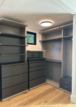 Custom walk-in closet with dark gray drawers, open shelving, hanging rods, and wood flooring.