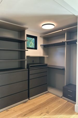 Custom walk-in closet with dark gray drawers, open shelving, hanging rods, and wood flooring.