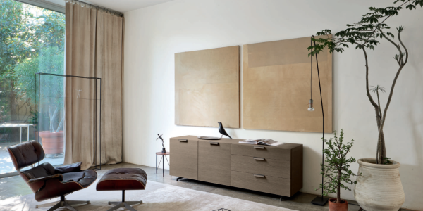 Modern Italian living room sideboard with dark wood cabinetry, open display shelving, textured wall tile, table lamp, framed artwork, and soft natural light.