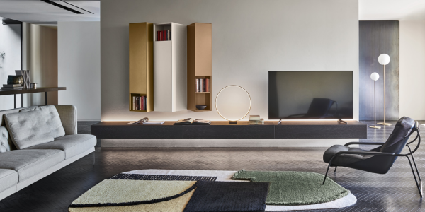 Modern Italian living room with low wood media cabinet, wall-mounted shelving, large TV, round mirror, lounge chair, indoor plant, and bright natural light.