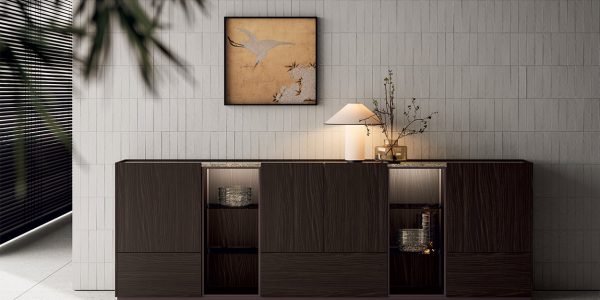 Modern Italian living room sideboard with dark wood cabinetry, open display shelving, textured wall tile, table lamp, framed artwork, and soft natural light.