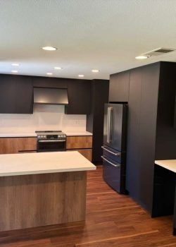 Completed modern kitchen with wood flooring, flat panel cabinetry, island seating, integrated appliances, and contemporary lighting.