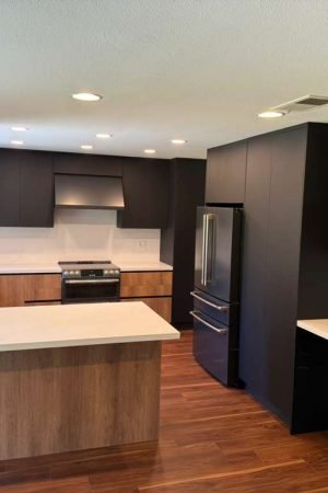 Completed modern kitchen with wood flooring, flat panel cabinetry, island seating, integrated appliances, and contemporary lighting.