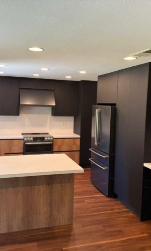 Completed modern kitchen with wood flooring, flat panel cabinetry, island seating, integrated appliances, and contemporary lighting.