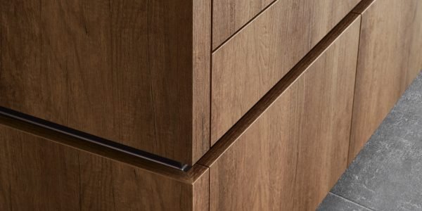 Close-up of warm wood textured melamine cabinet drawers with clean horizontal lines, integrated handle detailing, and modern kitchen styling.