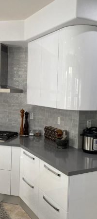 White corner kitchen with glossy cabinetry, gray tile backsplash, stainless range hood, gas cooktop, and dark countertop.