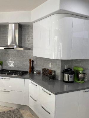 White corner kitchen with glossy cabinetry, gray tile backsplash, stainless range hood, gas cooktop, and dark countertop.