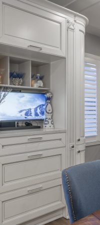 White built-in cabinetry with glass display cabinet, integrated media storage, detailed molding, and a bright traditional interior style.
