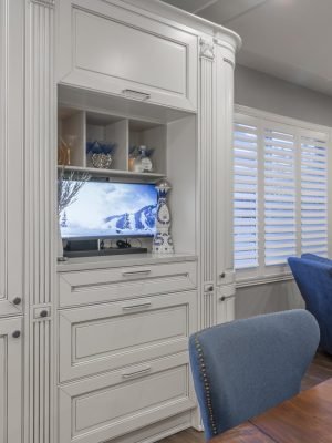 White built-in cabinetry with glass display cabinet, integrated media storage, detailed molding, and a bright traditional interior style.